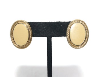 May include: A pair of gold oval-shaped clip-on earrings with a cream-colored center.
