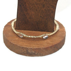 Könnte beinhalten: Goldenes Armreif-Armband mit klaren ovalen Steinen. Das Armband befindet sich auf einem Holzständer.