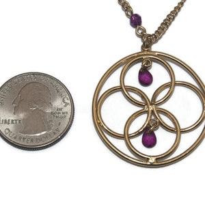 May include: Gold necklace with a circular pendant featuring four interlocking circles and three dangling purple gemstones.