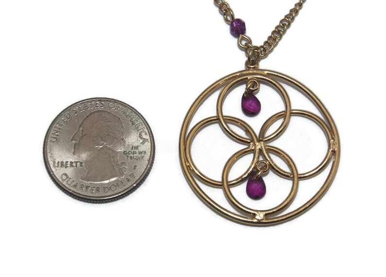 May include: Gold necklace with a circular pendant featuring four interlocking circles and three dangling purple gemstones.