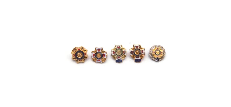 K&ouml;nnte beinhalten: F&uuml;nf verzierte, goldfarbene Broschen mit aufwendigen Designs und farbenfrohen Akzenten. Jede Brosche hat ein zentrales Emblem, das von einem detaillierten Rand umgeben ist, mit roten, blauen und wei&szlig;en Emaille-Details. Die Broschen sind auf wei&szlig;em Hintergrund angeordnet.