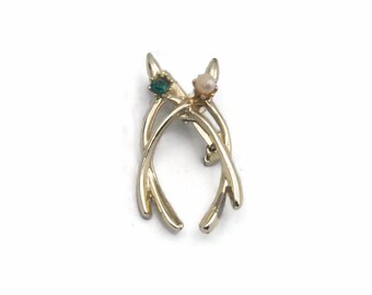 Puede incluir: Broche de tono dorado con un par de astas, adornada con una piedra verde y una piedra blanca.