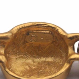 May include: Close-up of a gold-toned metal chain with a round link featuring the inscription "&copy; AK".