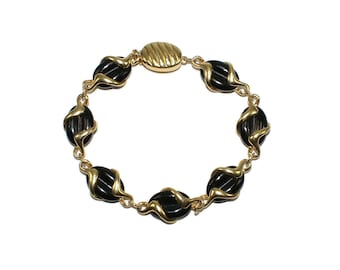 May include: A gold bracelet with black oval-shaped links. The bracelet has a gold clasp with a decorative design.