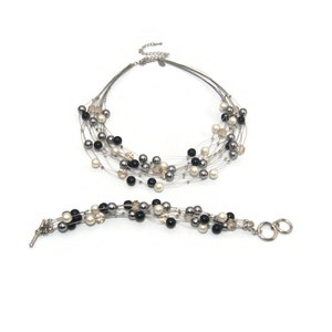Pode incluir: Um conjunto de colar e pulseira de prata com contas pretas, brancas e cinzas. O colar é de várias camadas e a pulseira tem um fecho.