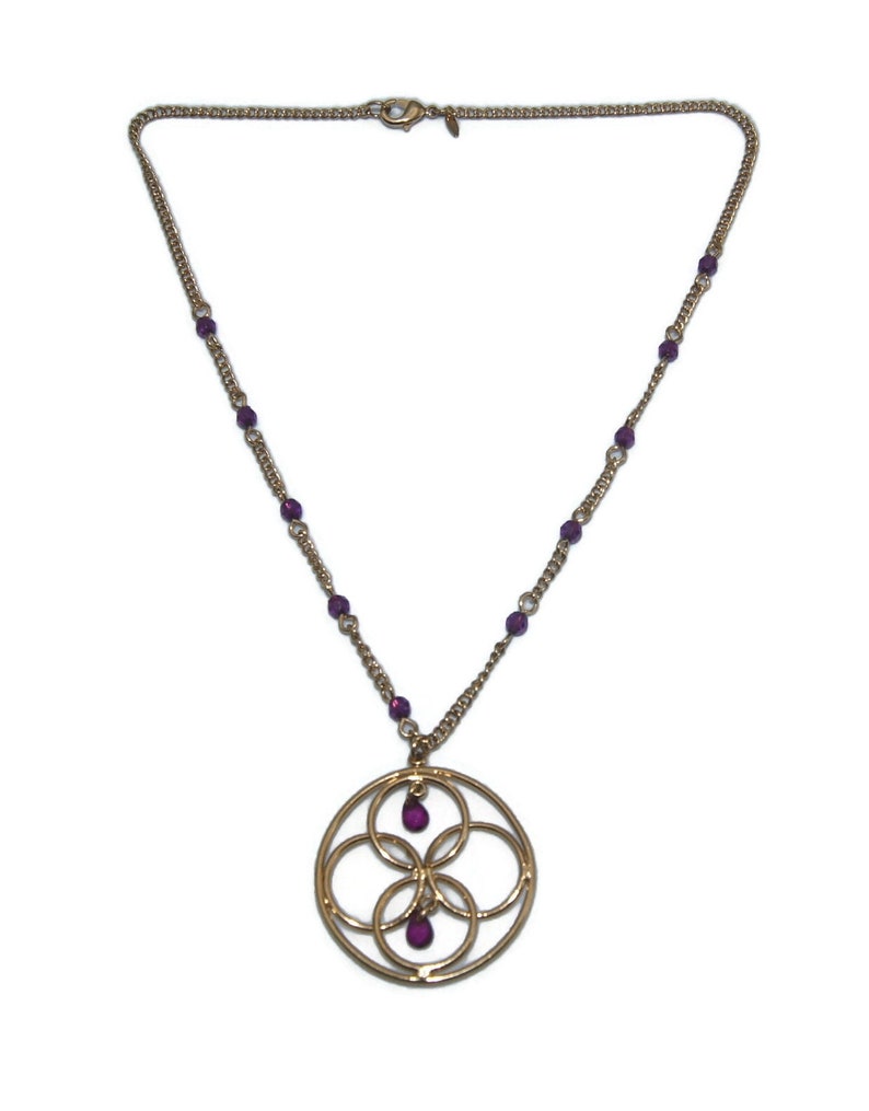 May include: A gold chain necklace with a circular pendant featuring an intricate design of overlapping circles. The pendant has three small purple gemstones.