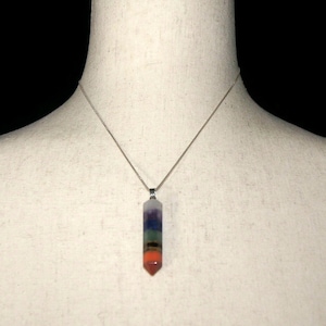 May include: A silver chain necklace with a seven-chakra crystal pendant. The pendant is a pointed, clear crystal with seven bands of color, representing the seven chakras.
