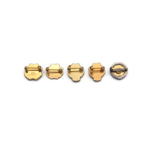 K&ouml;nnte beinhalten: F&uuml;nf Broschen im Vintage-Stil mit Anstecknadeln sind in einer Reihe angeordnet. Die Broschen haben goldfarbene Metallrahmen und dekorative Zentren. Die Designs umfassen florale und geometrische Formen mit einer Vielzahl von Farben und Texturen.