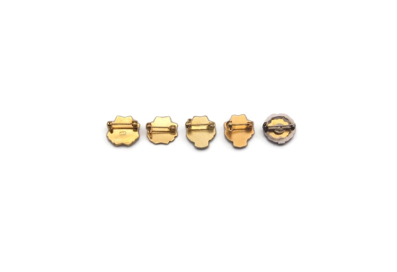 K&ouml;nnte beinhalten: F&uuml;nf Broschen im Vintage-Stil mit Anstecknadeln sind in einer Reihe angeordnet. Die Broschen haben goldfarbene Metallrahmen und dekorative Zentren. Die Designs umfassen florale und geometrische Formen mit einer Vielzahl von Farben und Texturen.