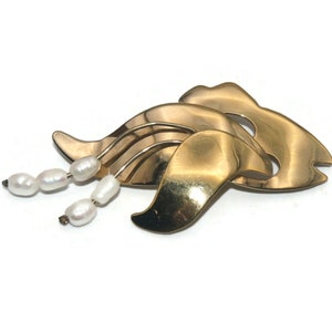 May include: A gold-toned brooch with a stylized wave design and a dangling strand of faux pearls.
