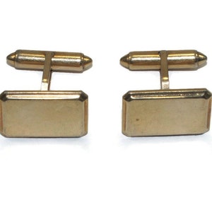May include: A pair of gold-toned cufflinks with a rectangular shape. The cufflinks have a smooth, polished finish.