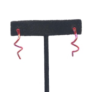 May include: A pair of spiral earrings with a gradient of red to purple hues. The earrings are displayed on a black earring stand against a white background. The earrings have a unique, abstract design.