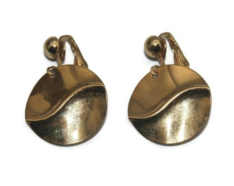 May include: A pair of gold-tone clip-on earrings with a wavy, textured design. The earrings are round and have a smooth, polished finish.