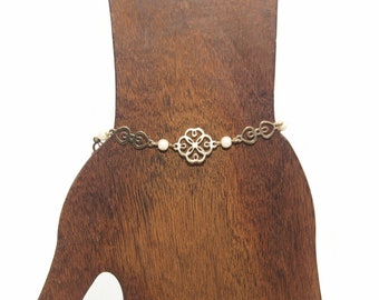 May include: A gold chain bracelet with a delicate, intricate design featuring a four-leaf clover charm and small white beads.