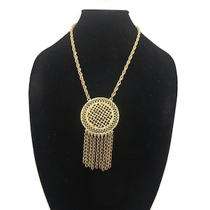 May include: A gold necklace with a large, round pendant featuring a woven design and a fringe of chains.
