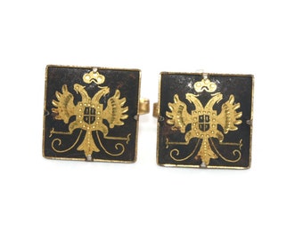 May include: A pair of gold cufflinks with a black enamel background. The cufflinks feature a gold double-headed eagle design with a shield in the center.