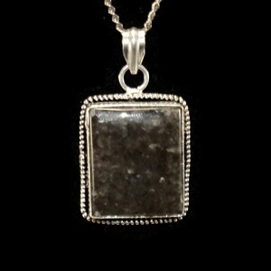 May include: A silver chain necklace with a square pendant featuring a dark gray stone with a speckled pattern.