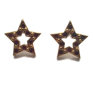 Puede incluir: Un par de pendientes de estrella de oro con un borde de pedrería roja.