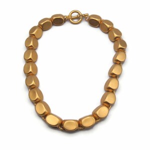 May include: A gold-toned necklace made of large, rounded, matte beads. The necklace has a simple clasp.