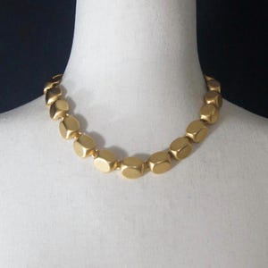 May include: A gold necklace made of large, rounded, geometric beads.