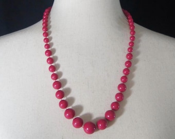 Peut inclure: Un collier composé de perles rondes rose vif. Le collier est sur un mannequin blanc.