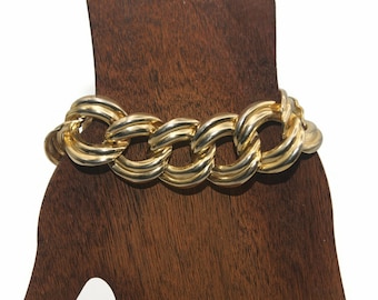 May include: A gold chain bracelet with large, thick links. The bracelet is made of a shiny metal and has a chunky, bold design.