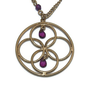 May include: Gold necklace with a circular pendant featuring an intricate design of overlapping circles and two dangling purple gemstones.