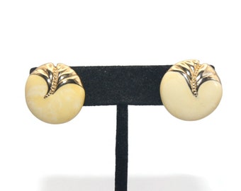 May include: A pair of gold tone clip-on earrings with a white, round, textured design. The earrings have a gold tone leaf design on the front.