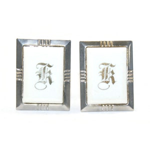 Peut inclure: Une paire de boutons de manchette en argent avec un insert en porcelaine blanche représentant la lettre "K" en écriture dorée.