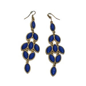 Puede incluir: Un par de pendientes largos y colgantes con una cadena dorada y piedras azules en forma de lágrima. Los pendientes están hechos de metal y tienen un diseño delicado y femenino.