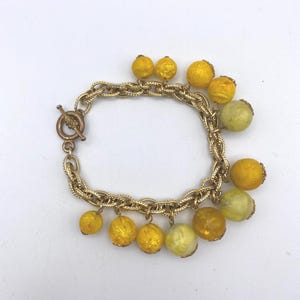 May include: Gold-toned bracelet featuring a chain design with a toggle clasp. The bracelet is adorned with multiple yellow and light green beaded charms. The beads vary in size and texture, adding visual interest to the jewelry.