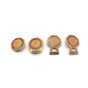 May include: Four gold-toned vintage pins with blue and gold detailing. The pins have an octagonal shape with intricate designs and text. Two pins have a stand. The pins are displayed on a white background.