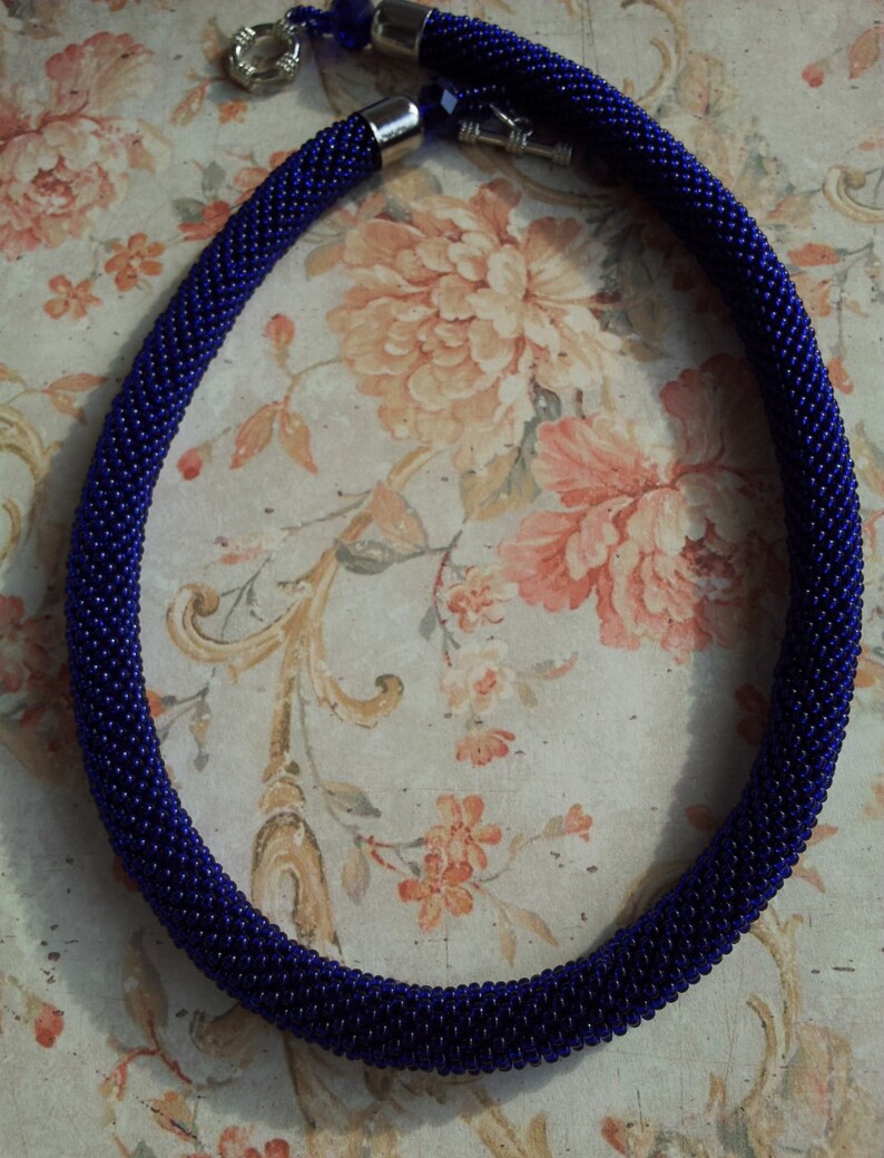 May include: A dark blue beaded necklace with silver clasps. The necklace is made of small, round beads and is about 18 inches long.