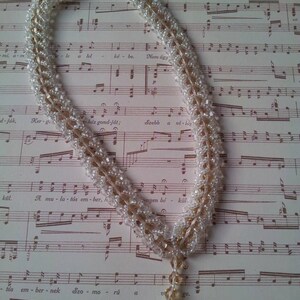 May include: A white and gold beaded necklace with a crystal pendant hanging from it. The necklace is lying on a sheet of music.