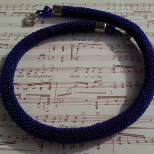 May include: A close-up of a dark blue beaded necklace with silver clasps. The necklace is lying on a sheet of music.