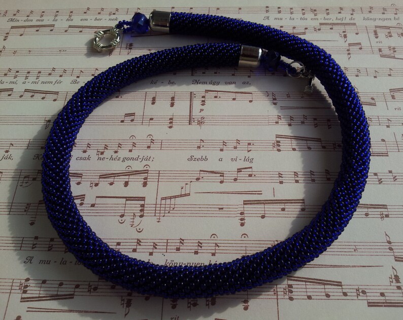 May include: A close-up of a dark blue beaded necklace with silver clasps. The necklace is lying on a sheet of music.