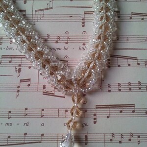 May include: A delicate necklace made of clear and brown glass beads. The necklace is layered and features a teardrop-shaped pendant.