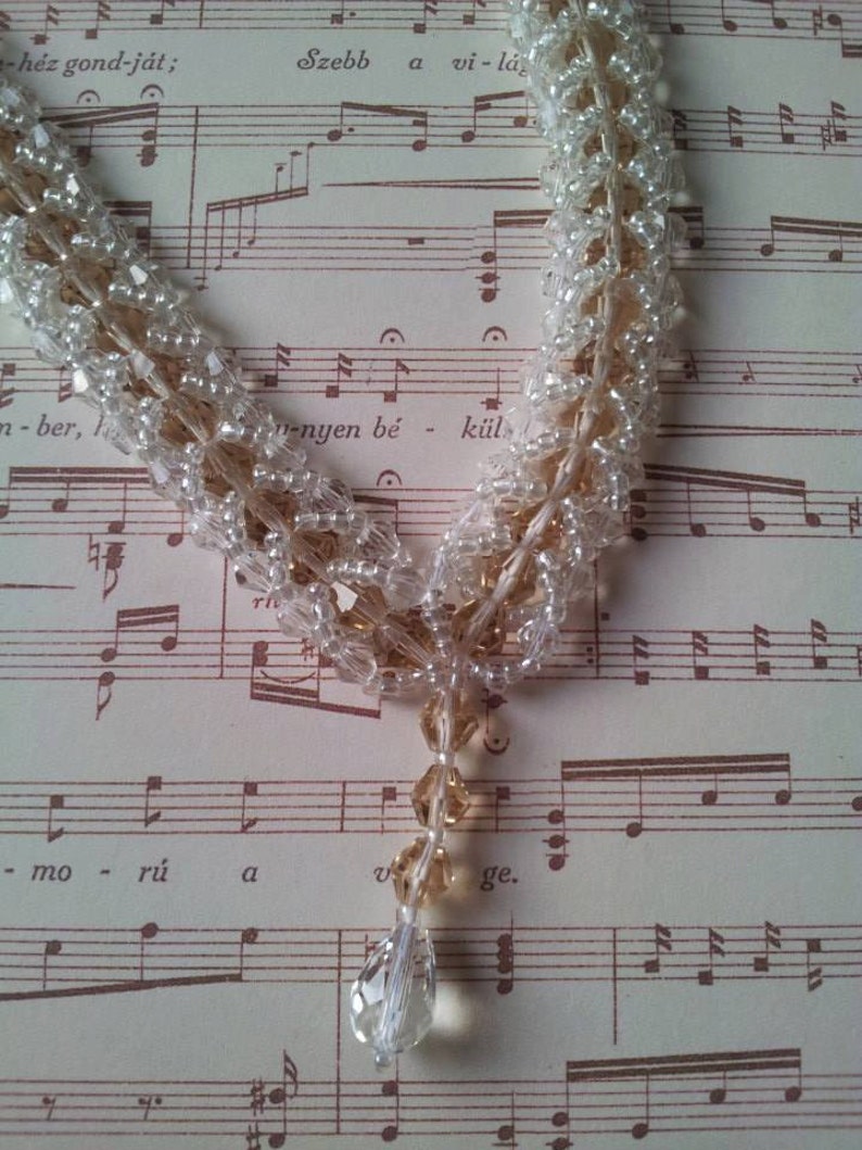 May include: A delicate necklace made of clear and brown glass beads. The necklace is layered and features a teardrop-shaped pendant.