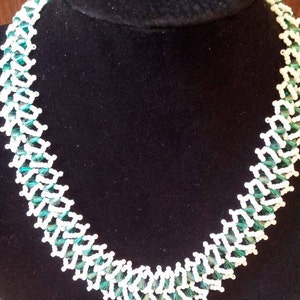 May include: A white and green beaded necklace with a geometric pattern. The necklace is made of small, faceted beads that are strung together in a repeating pattern.