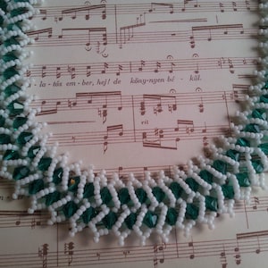 May include: A white and green beaded necklace with a chevron pattern. The necklace is made with small, faceted beads.