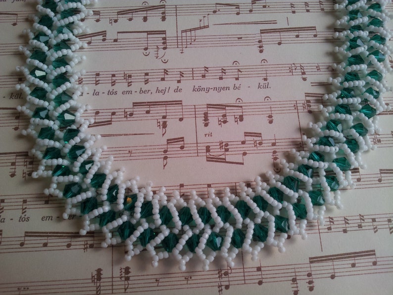 May include: A white and green beaded necklace with a chevron pattern. The necklace is made with small, faceted beads.