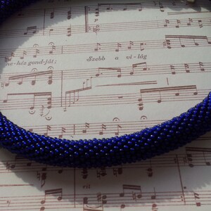 May include: A dark blue beaded necklace made of small, round beads. The necklace is coiled and lying on a sheet of music.