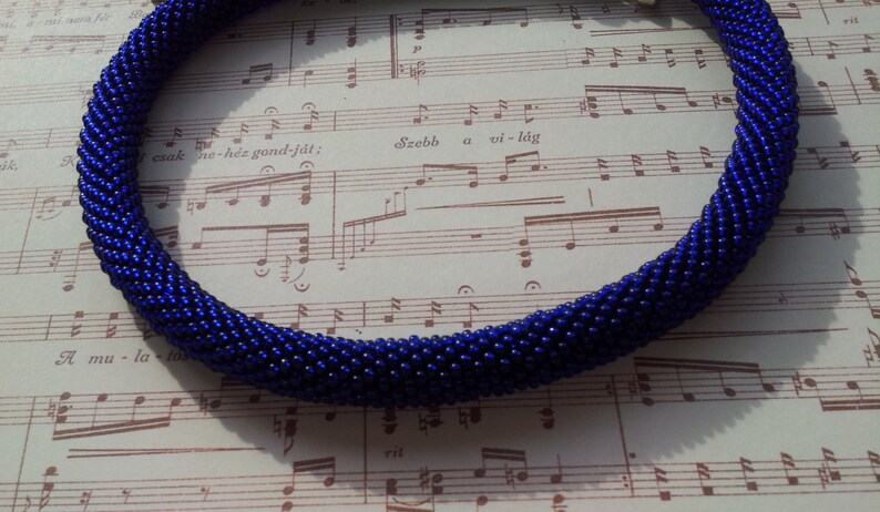 May include: A dark blue beaded necklace made of small, round beads. The necklace is coiled and lying on a sheet of music.