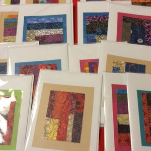 May include: A collection of handmade greeting cards featuring colorful fabric scraps arranged in a patchwork style. The cards are blank inside and ready for a personal message.