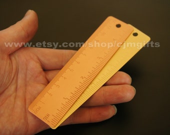 May include: Two metal rulers, one orange and one yellow, with inch markings. The rulers are held in a hand.