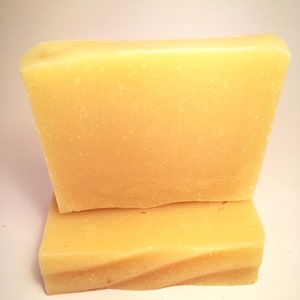 May include: Two bars of pale yellow soap stacked on top of each other. The soap is rectangular and has a smooth, slightly textured surface.