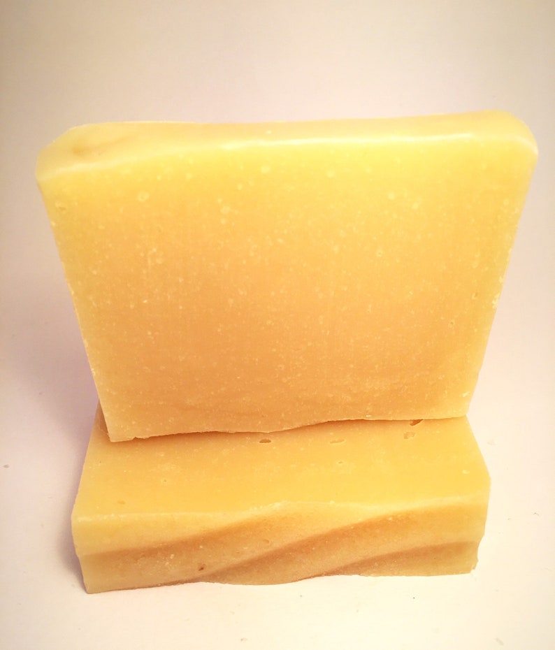 May include: Two bars of pale yellow soap stacked on top of each other. The soap is rectangular and has a smooth, slightly textured surface.