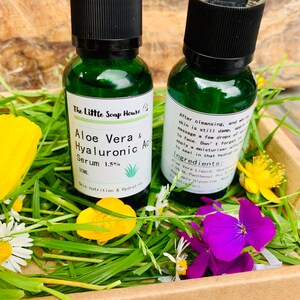 Puede incluir: Dos peque&ntilde;os frascos de vidrio verde con goteros que contienen un l&iacute;quido transparente. Los frascos est&aacute;n etiquetados con "Aloe Vera & Hyaluronic Acid Serum 1.5%" y "The Little Soap House". Los frascos est&aacute;n sobre un lecho de hierba verde y flores.