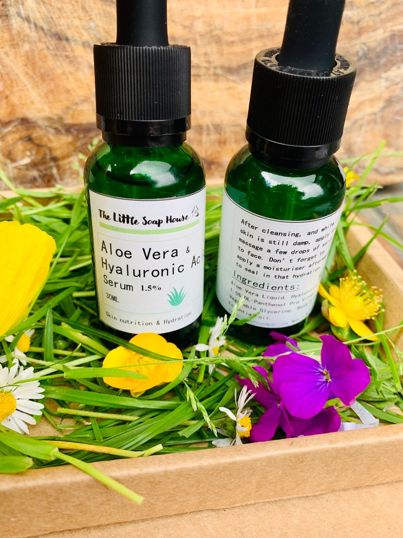 Puede incluir: Dos peque&ntilde;os frascos de vidrio verde con goteros que contienen un l&iacute;quido transparente. Los frascos est&aacute;n etiquetados con "Aloe Vera & Hyaluronic Acid Serum 1.5%" y "The Little Soap House". Los frascos est&aacute;n sobre un lecho de hierba verde y flores.