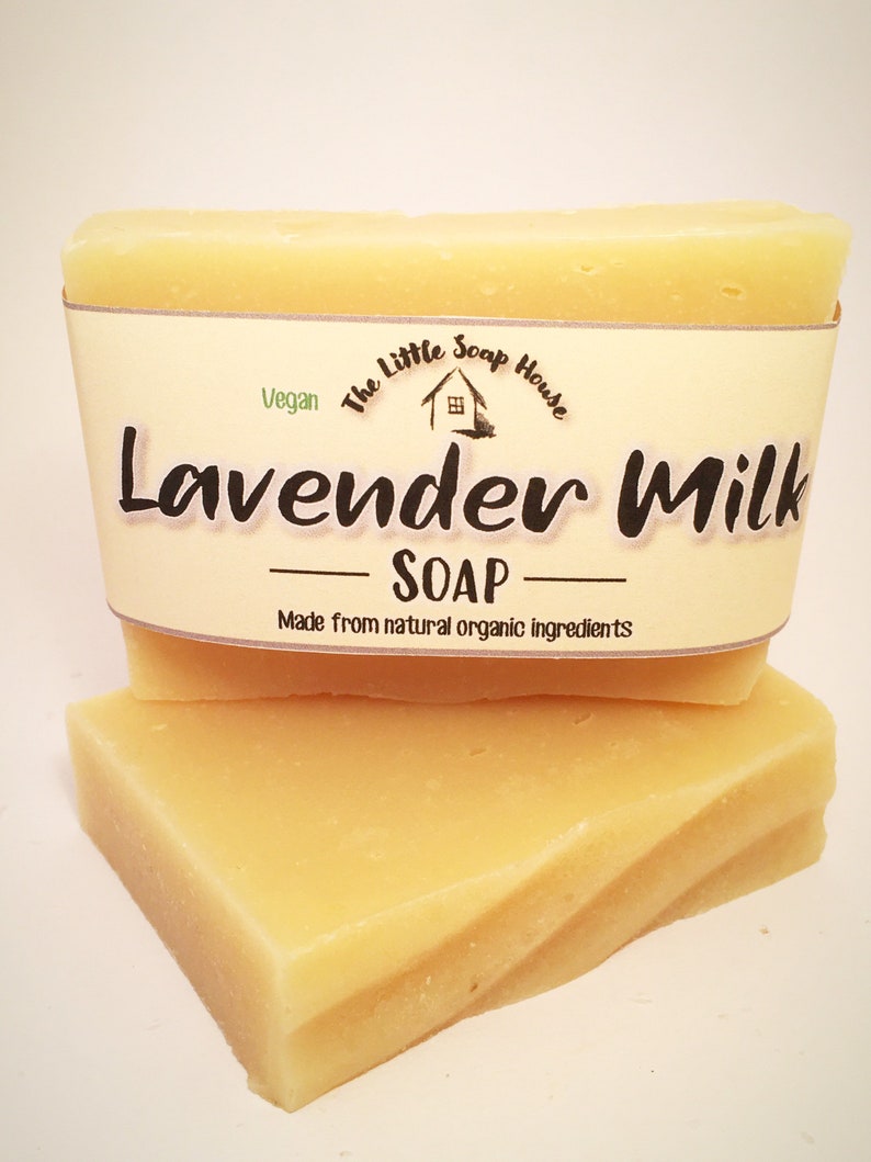 May include: Two bars of pale yellow soap stacked on top of each other. The top bar has a label that reads "The Little Soap House" with a small house icon and "Vegan" in green text. The label also says "Lavender Milk - SOAP - Made from natural organic ingredients".